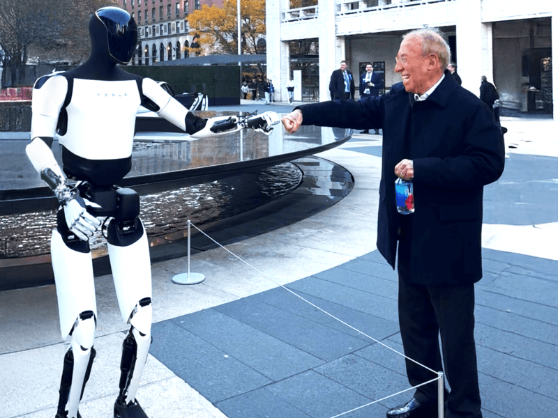 A photo of Ron Baron fist bumping Optimus at the 32nd Annual Baron Investment Conference